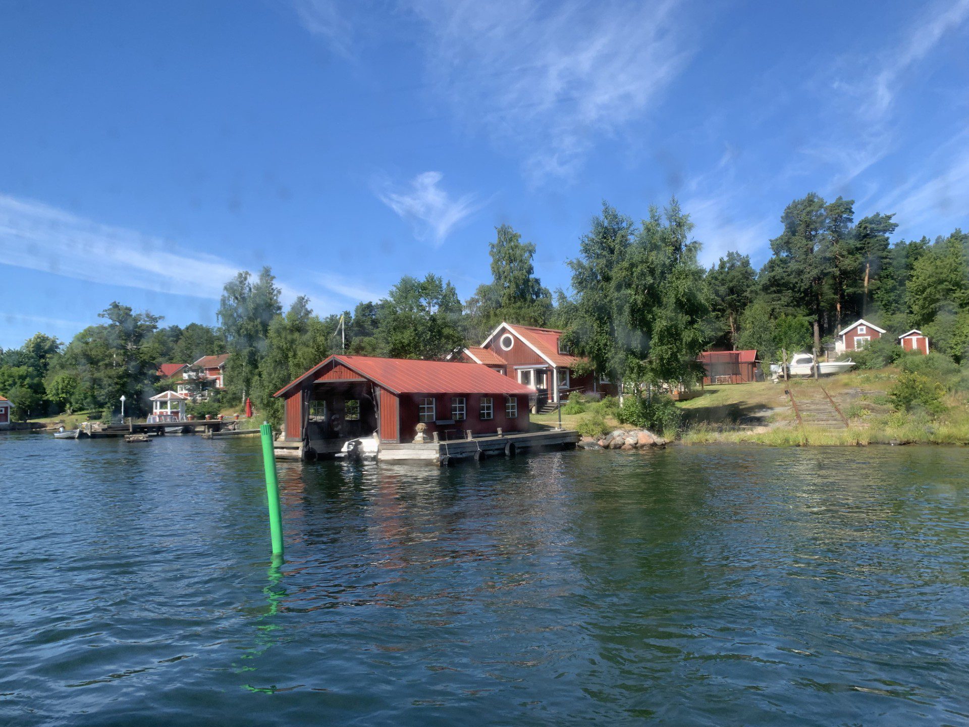Lokala experter på RIB‑upplevelser i Stockholms skärgård Traditional red wooden houses along the shoreline in the Stockholm archipelago, viewed from the water during a private RIB charter with 59 DEGREES NORTH.