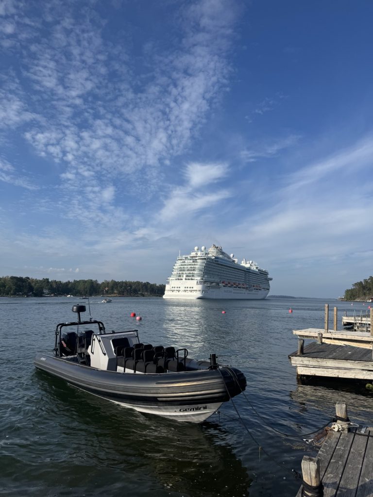 Skärgårdsupplevelser med RIB‑båt i Stockholms skärgård Gemini WR 880 - RIB speedboat moored in the Stockholm archipelago with a cruise ship passing in the background, illustrating fast and exclusive archipelago experiences with 59 Degrees North