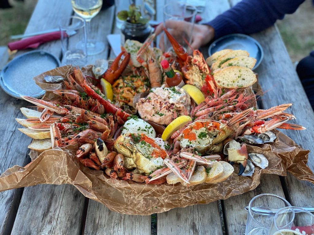 Lyxig RIB‑tur i Stockholms skärgård & Ingmarsö Krog Luxury seafood platter from Möja Fisk (Les Poissonniers de Möja) in Stockholm archipelago featuring lobster, langoustines, shrimp, oysters and fresh bread served outdoors.